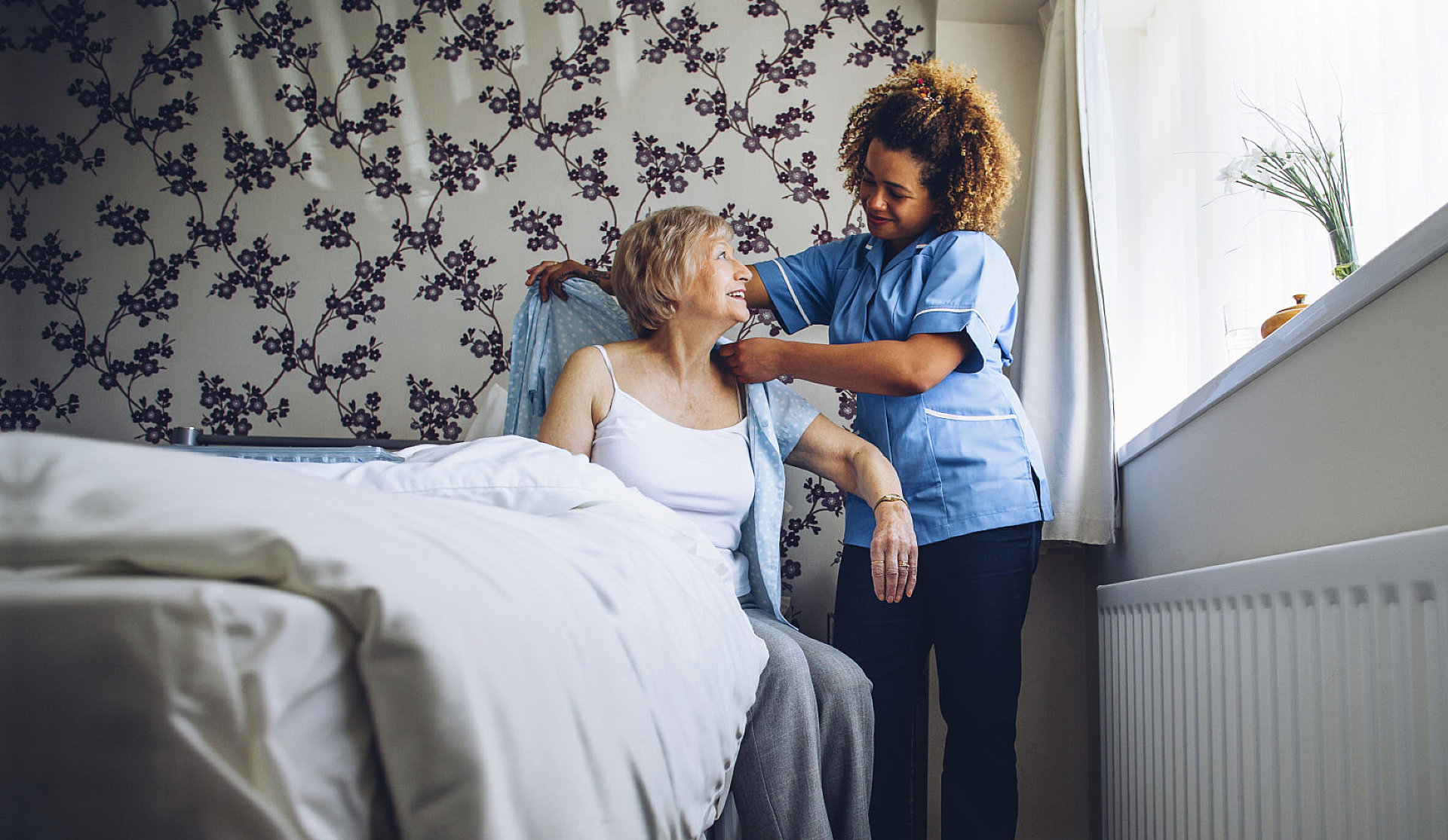 caretaker helps elder lady dress up