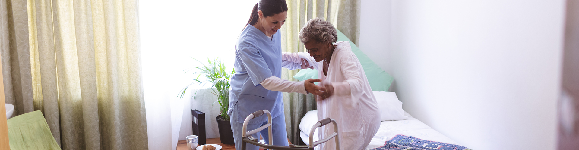 caretaker helping elder lady stand from bed